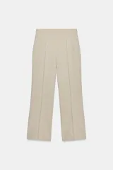 Pantalón de vestir color beige claro, tiro alto, corte recto o ligeramente acampanado, con pinzas marcadas en el frente y bolsillos delanteros.
