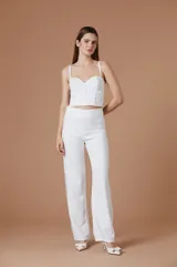 Pantalón de mujer blanco de corte sastrero, tiro alto y silueta amplia de pernera recta con detalles de flecos o pedrería en los laterales.