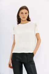 Remera blanca de lino de textura suave y liviana, con calce al cuerpo y mangas cortas. Presenta cadenas de strass decorativas en los hombros.