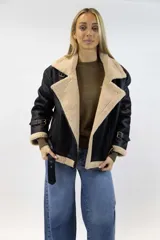 Campera oversize de efecto cuero color marrón con interior, solapas, cuello y puños de corderito sintético en tono tostado. Cuenta con detalles de tiras ajustables con hebilla en el cuello, mangas y ruedo, y cierre frontal cruzado.