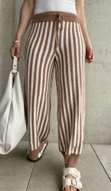 Pantalón tejido a rayas verticales color marrón y blanco, con cintura y tobillos acanalados con cordón ajustable.