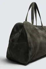 Bolso de viaje de gran tamaño confeccionado en piel con acabado de serraje. Cuenta con un compartimento principal con cierre de cremallera e imanes, interior con bolsillo con cierre y bolsillo plano, y dos asas de mano de piel.