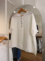 Blusa oversize de lino color blanco, con cuello redondo, mangas cortas y cartera frontal con botones oscuros.