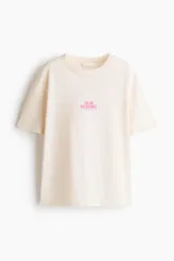 Remera oversized en punto de algodón color beige, de cuello redondo y manga corta, con estampa frontal pequeña en tono rosado con la inscripción "Solar Treasures".