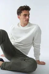 Buzo de felpa color crudo, de corte recto, con cuello redondo, puños y ruedo acanalados.