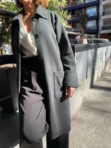 Saco largo gris oscuro tejido en lana merino, con cuello, puños y bolsillos de tejido con diseño de espiga en tono gris claro.