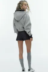 Cazadora de estilo deportivo con capucha ajustable, cierre frontal de doble cremallera y mangas abullonadas con puños elásticos. Presenta bolsillos delanteros y bajo elástico.