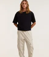 Pantalón cargo recto color beige, con cintura elástica ajustable con cordón, bolsillos laterales tipo cargo con solapa y bolsillos con cremallera.