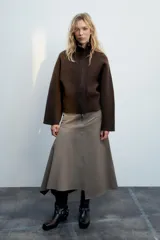 Chaqueta de punto marrón de textura bouclé, con cuello subido, manga larga ancha y cierre frontal oculto con cremallera.