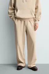 Pantalón jogger de corte relajado y pernera ancha, confeccionado en tejido de algodón con interior perchado. Presenta cintura elástica con cordón interior, bolsillos laterales y un bolsillo trasero de plastrón.