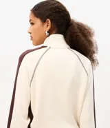Campera deportiva de cuello alto con cierre frontal y bolsillos tipo canguro, en color beige con detalles marrones en las mangas y estampa localizada con texto "Phoenix Arizona".