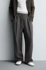 Pantalón de corte relajado, color gris oscuro, con cintura elástica ajustable mediante cordón y pliegues frontales. Presenta bolsillos laterales y bolsillos traseros de parche con pespuntes contrastantes.