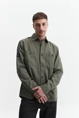 Sobrecamisa verde militar de twill de algodón, con cuello clásico, cierre frontal con botones a tono, dos bolsillos tipo parche con solapa abotonada en el pecho, mangas largas con puños abotonados y corte recto.