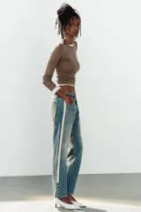 Jeans rectos de tiro medio en denim azul con efecto deslavado. Presentan bandas laterales con detalles brillantes, bolsillos delanteros y traseros, y aberturas en los tobillos con botonadura metálica.