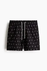 Short de baño negro de sirsaca con estampado de palmeras blancas, cintura elástica con cordón de ajuste blanco y bolsillos laterales.