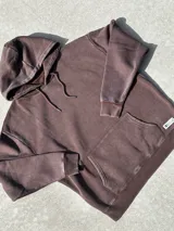 Buzo canguro marrón con capucha y cordones, de corte amplio y estilo urbano.