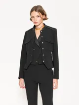 Chaqueta negra con cuello mao y charreteras de cuero ovino tableado en los hombros. Tiene acceso mediante broches forrados de cuero, bolsillos delanteros plaqué con tapa y fuelle, y godet en la espalda baja.