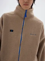 Campera de sherpa color beige con cuello alto, cierre frontal a contratono en color azul y bordado de la marca Pastiche en el pecho.