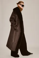 Abrigo largo de Zara Woman Collection en color marrón chocolate, con cuello de solapa amplio, mangas largas y cinturón ajustable del mismo tejido. Presenta detalles de forro interior y acabados en efecto pelo a tono en cuello, puños y bordes frontales.