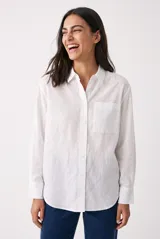 Camisa blanca de corte clásico, manga larga con puños anchos abotonados, cuello camisero, cierre frontal con botones y un bolsillo aplicado en el pecho.