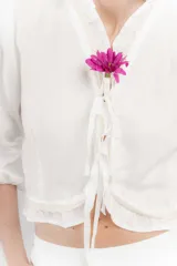 Blusa corta blanca de lino con mangas 3/4 abullonadas, escote en V con volados y cierre con lazos.