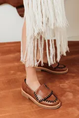 Mocasines de cuero marrón con diseño artesanal, detalle de costuras trenzadas en contraste en la parte frontal y suela baja con taco cómodo.
