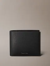 Billetera bifold Calvin Klein confeccionada en piel con textura saffiano. Cuenta con compartimento para billetes, múltiples ranuras para tarjetas y monedero interno. Presenta logo metálico de la marca en el frente.
