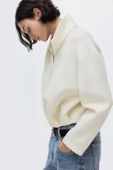 Campera color crema con efecto neopreno, cuello chimenea y cierre frontal. Presenta hombros caídos y pliegues en el bajo.