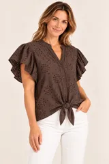 Blusa marrón de algodón con diseño de broderie, mangas cortas con volados y cierre frontal de botones con detalle de nudo en el dobladillo.