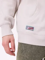 Canguro gris claro con capucha y estampado trasero en azul. El estampado incluye el texto "Spirit League Rusty Team" y una ilustración de una camioneta con animales y tablas de surf.