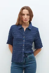 Camisa de manga corta con textura de punto smock, cuello clásico y cierre frontal con botones dorados.