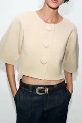 Chaqueta corta de punto color azul marino, de cuello redondo, manga por debajo del codo y cierre frontal con botones forrados al tono.