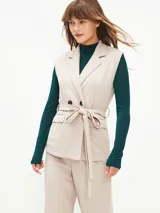 Chaleco beige con solapas, doble botonadura, lazo para atar en la cintura y bolsillos delanteros.