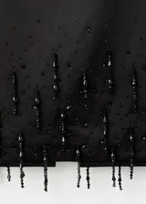 Falda midi recta de color negro, confeccionada en poliéster con forro interior, que presenta un detalle de adorno con cristales colgantes en el bajo.