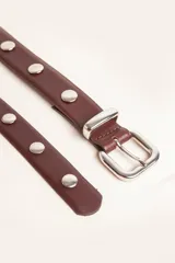 Cinto de cuero color suela con tachas metálicas circulares y hebilla plateada.