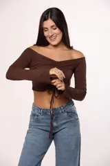Top de algodón color marrón, con escote off-shoulder, mangas largas y detalle de frunce central con lazo ajustable.