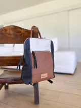 Mochila de cuero tricolor en tonos marrón tostado, negro y blanco, con bolsillo frontal con cierre, tiradores de cuero y detalle de etiqueta con logo grabado.