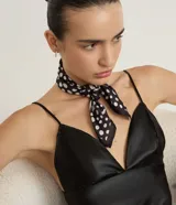 Pañuelo triangular de satén color negro con estampado de lunares blancos. Confeccionado en poliéster con acabado brillante y suave.