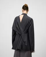 Blazer gris melange de corte holgado con solapa de muesca y cierre frontal de un solo botón. Presenta mangas largas con detalle de organza transparente en los puños y un diseño en la espalda con cruces, drapeados y aberturas. Confeccionado en una mezcla de poliéster y lana merino.
