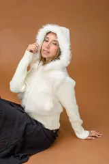 Campera corta de diseño combinado en color marrón. Presenta cuerpo de piel sintética con capucha, mangas tejidas en punto acanalado y cierre frontal con vista de cuero sintético. Incluye detalles de pompones laterales en el ruedo.