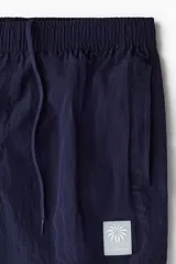 Short de baño de nylon azul marino con cintura elástica y cordón ajustable oculto, bolsillos laterales, bolsillo trasero con solapa y cierre autoadherente. Cuenta con suspensor interior de malla y un pequeño parche estampado en la pierna izquierda.