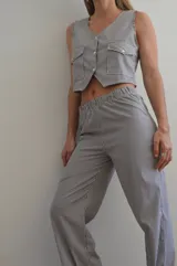 Chaleco a rayas verticales azules y blancas con cuello en V, cierre con botones y bolsillos frontales.