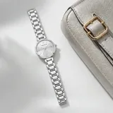 Reloj analógico de mujer con caja redonda y malla de eslabones metálicos en color plateado. Presenta esfera minimalista con índices finos y movimiento de cuarzo japonés.