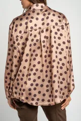 Camisa oversize de poliéster color rosa con estampado de lunares marrón oscuro, cuello camisero, cierre frontal de botones y mangas largas con puños elásticos.