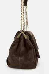 Bolso de hombro confeccionado en piel de gamuza color marrón, con diseño estructurado y pespuntes decorativos en la solapa. Cuenta con una correa de cadena metálica dorada con refuerzo de piel y cierre imantado.