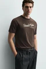 Camiseta regular fit color marrón oscuro, con cuello redondo y manga corta. Presenta un bordado frontal con el texto "Steam Lab" en blanco y una frase más pequeña debajo.
