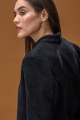 Chaqueta de corte entallado en color negro, confeccionada en un tejido suave con acabado ligeramente afelpado. Presenta un diseño minimalista sin botones, con cuello ligeramente elevado y mangas largas.