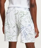 Bermuda de baño blanca con estampado floral de hojas de costilla de Adán en negro. Tiene cintura elástica con cordón ajustable y bolsillos laterales.