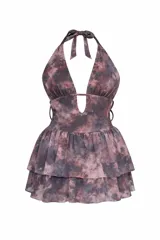 Vestido corto con estampado tie-dye en tonos gris y bordó, escote halter con lazo para atar al cuello y escote en V pronunciado con detalle de abertura en el centro. La falda es de dos capas con volados y tiene short incorporado.