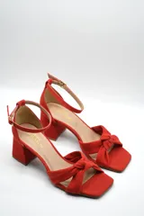 Sandalia de tacón medio ancho con diseño de nudo frontal y pulsera ajustable al tobillo con hebilla metálica.